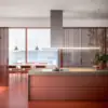 Falmec hood Lumen Island 175 Inox in a terracotta kitchen with sea view, showing the slim canopy and asymmetric left-side chimney
