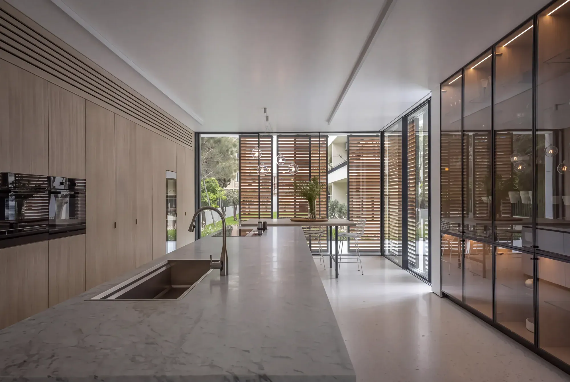 Kitchen by Wakim Group with a long marble island, oak tall units and louvered windows onto a garden
